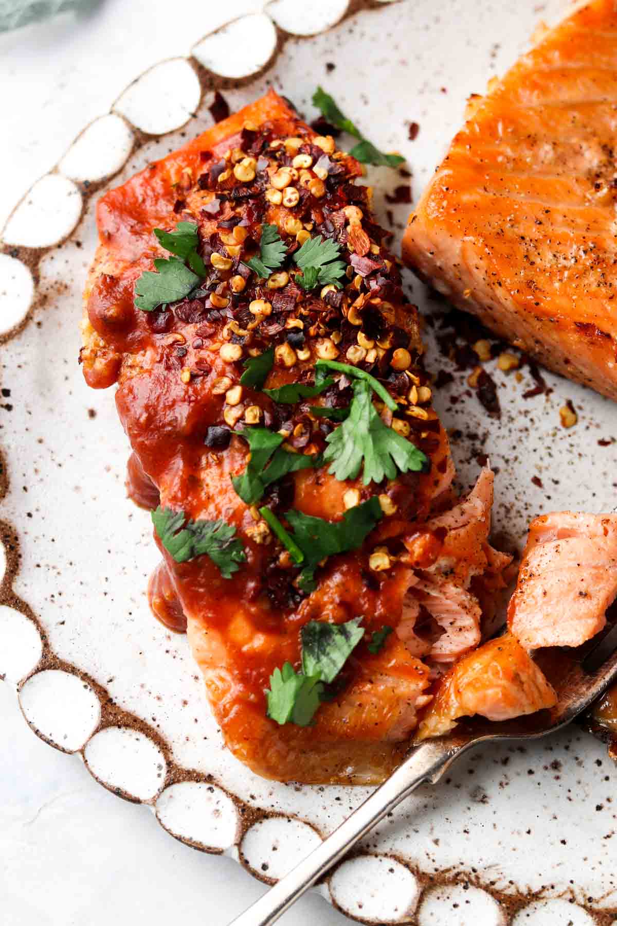 Picture of salmon on a white platter with sriracha sauce on top and fresh herbs. 