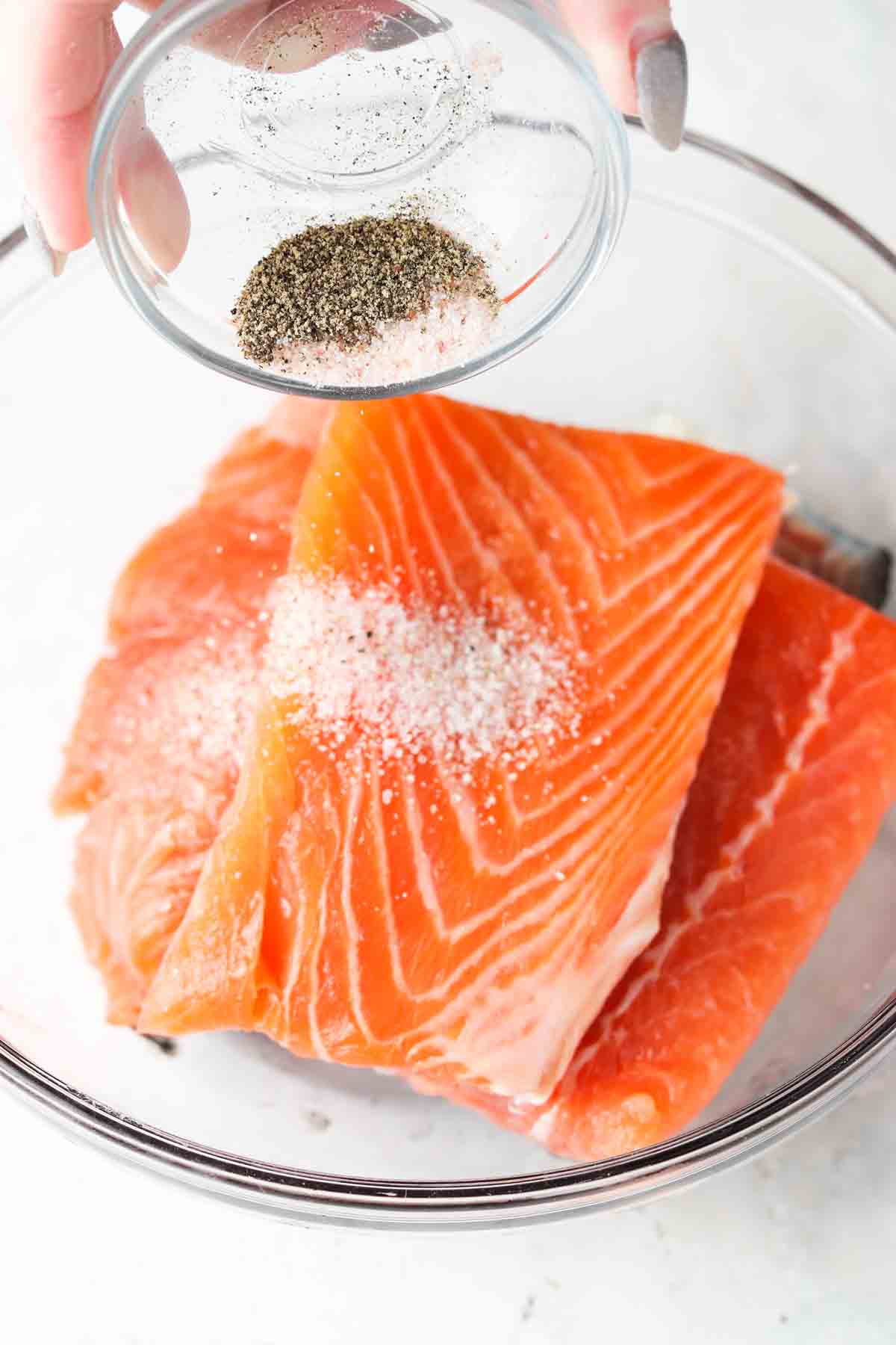 Frozen salmon filets in a glass bowl with salt and pepper sprinkled on top.