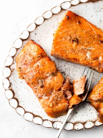 Air fried salmon filets on a white platter with freshly cracked pepper on top and a fork on the side.