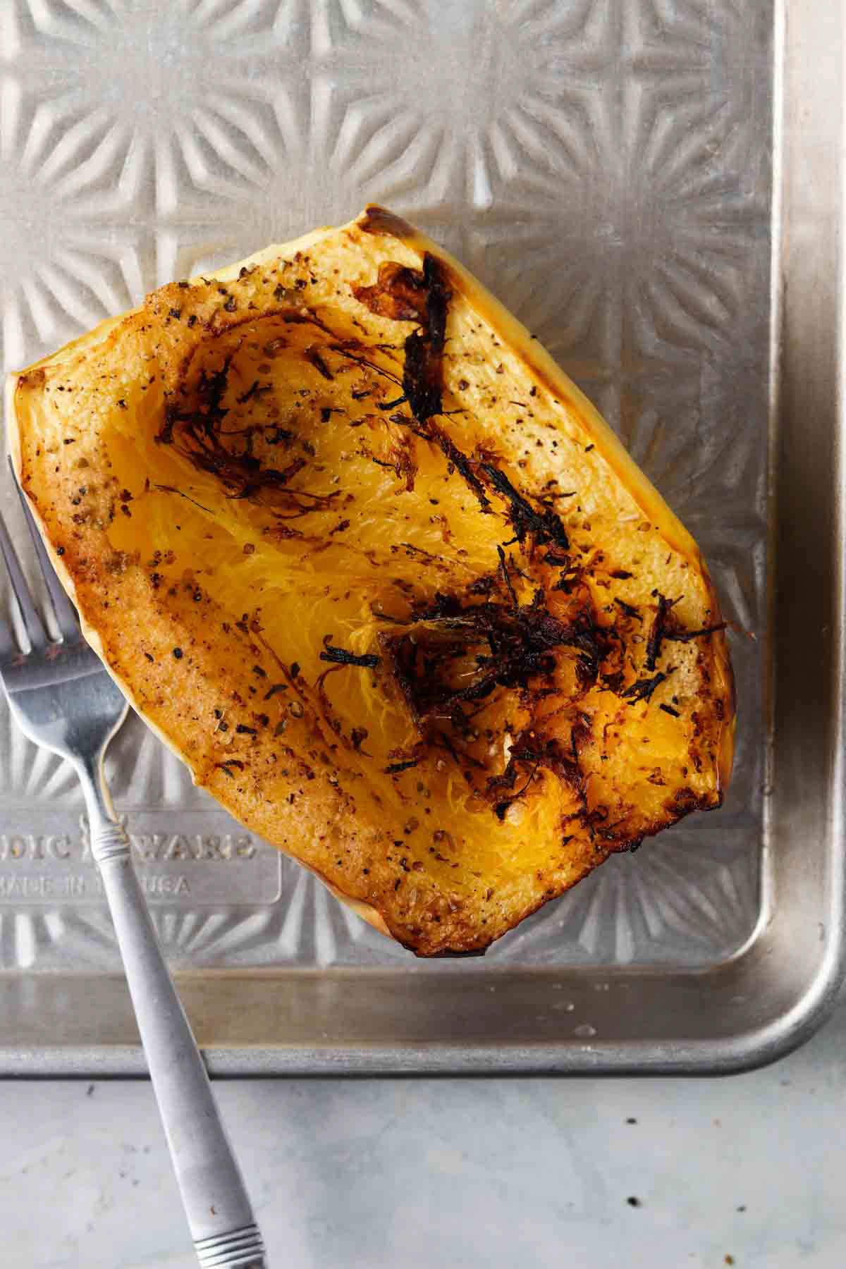 Cooked halved spaghetti squash on a baking tray with a fork next to it. 