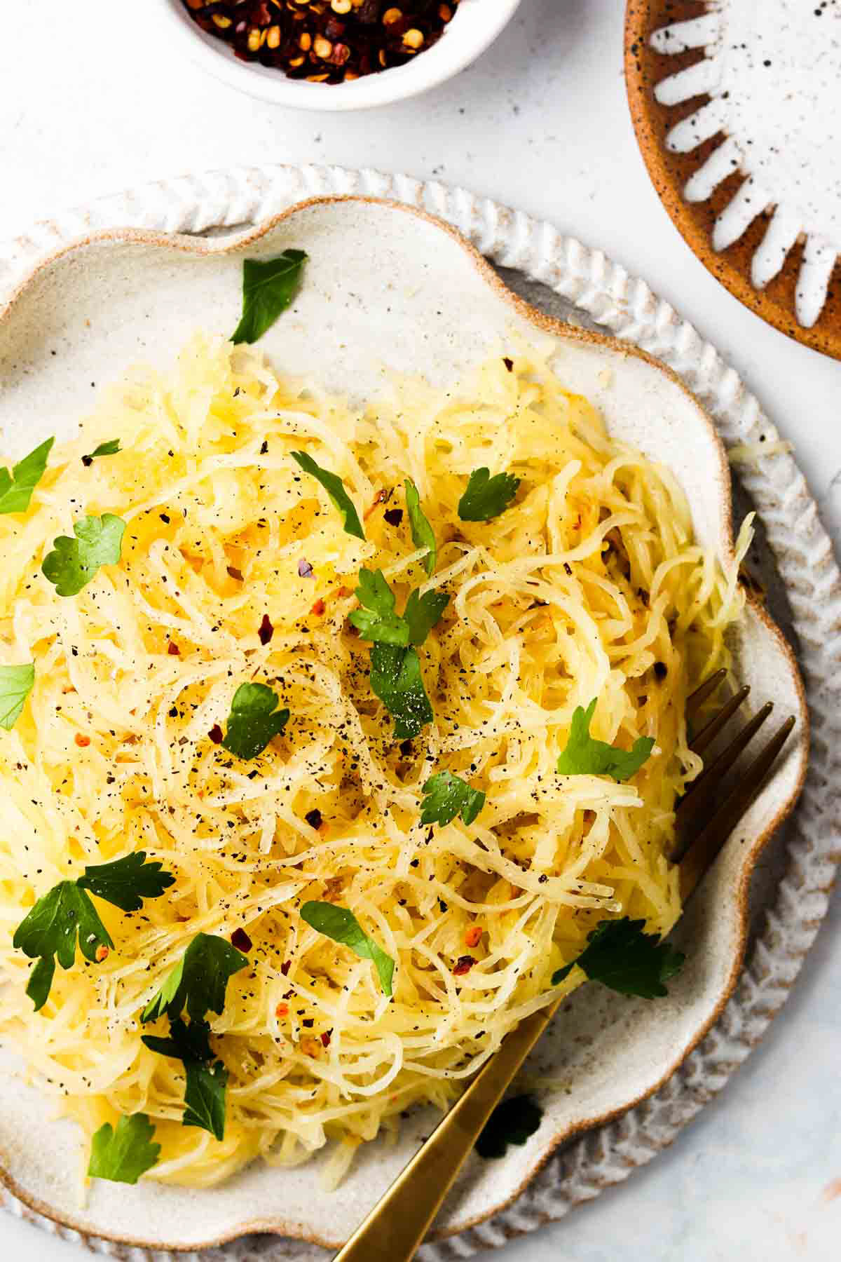 Cooked air fryer spaghetti squash on a tray and garnished with fresh green herbs and a gold fork.