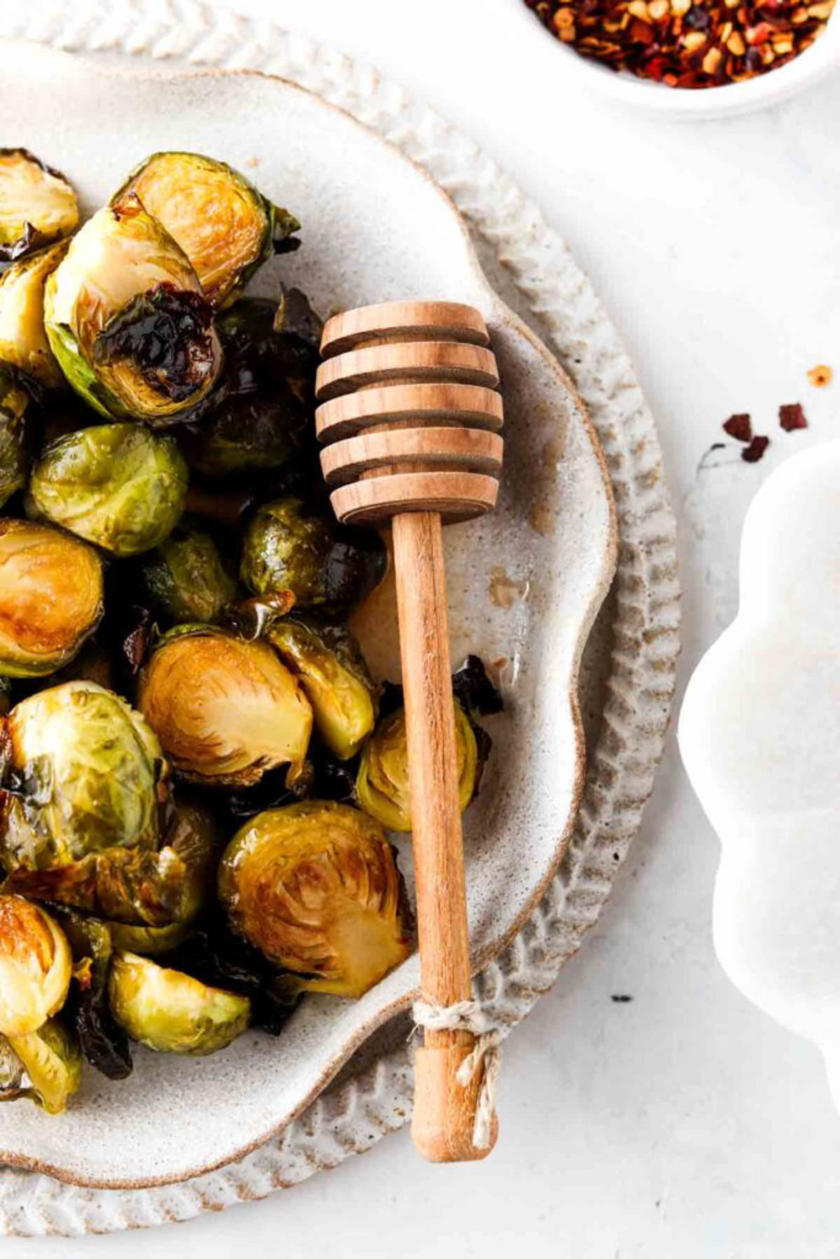 Honey sriracha brussel sprouts on a plate with a wooden honey comb.