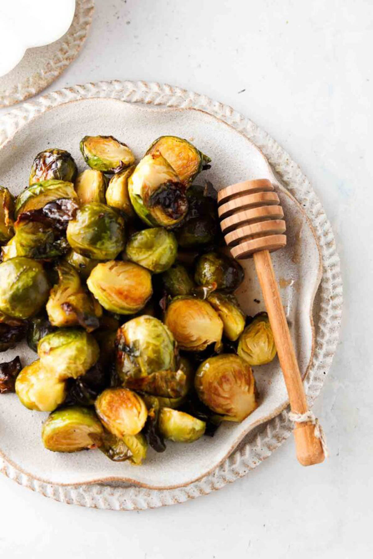 Honey sriracha brussel sprouts on a clay plate with a wooden honey comb beside it. 