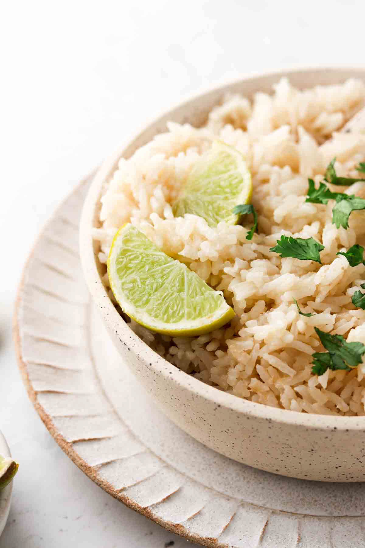 Coconut rice in a bowl with lime wedges and fresh green herbs.