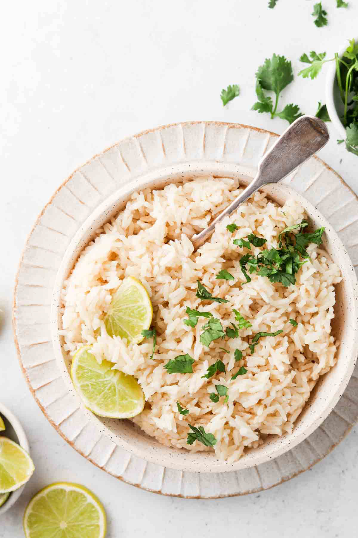 Coconut rice in a bowl with fresh limes and herbs on top.