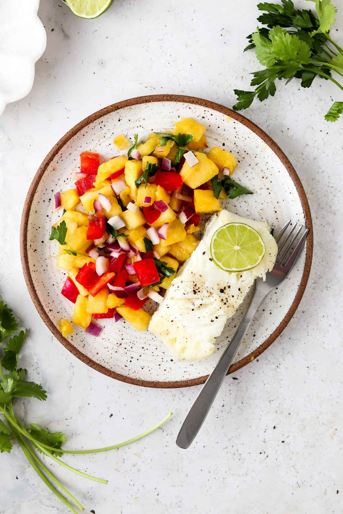 Pan seared sea bass with pico de gallo on a plate with lime.