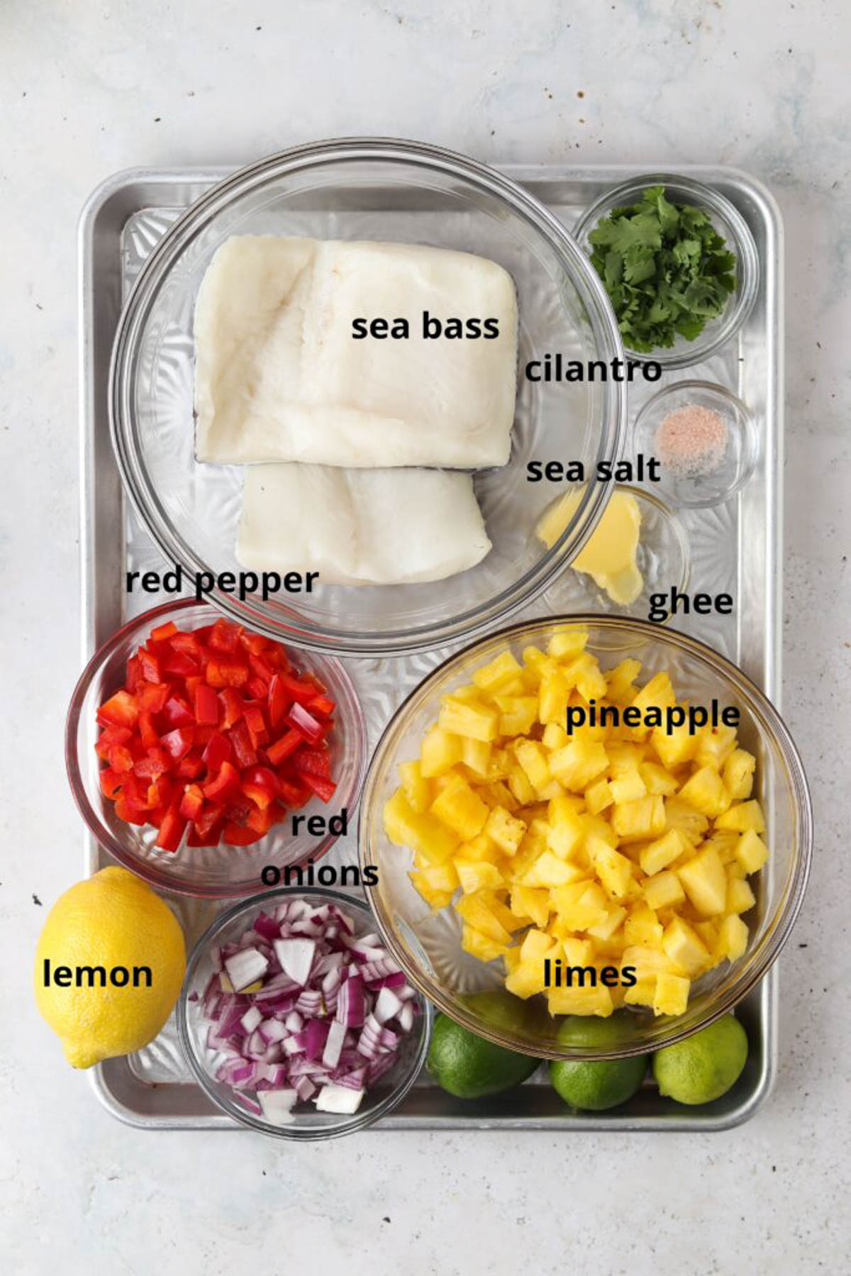 Pan seared sea bass with tropical pico de gallo ingredients in small glass bowls on a silver baking tray. 