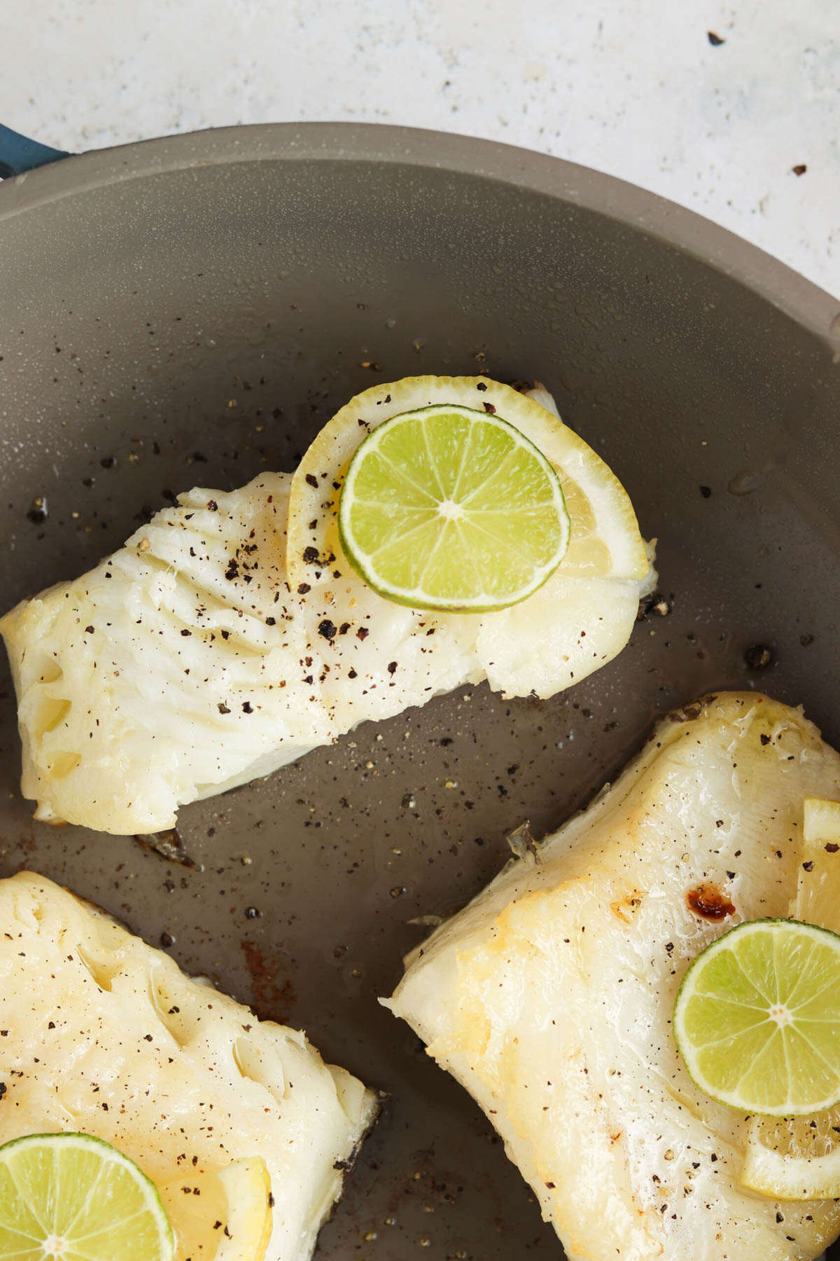 Seasoned sea bass in a skillet with lime slices on top. 