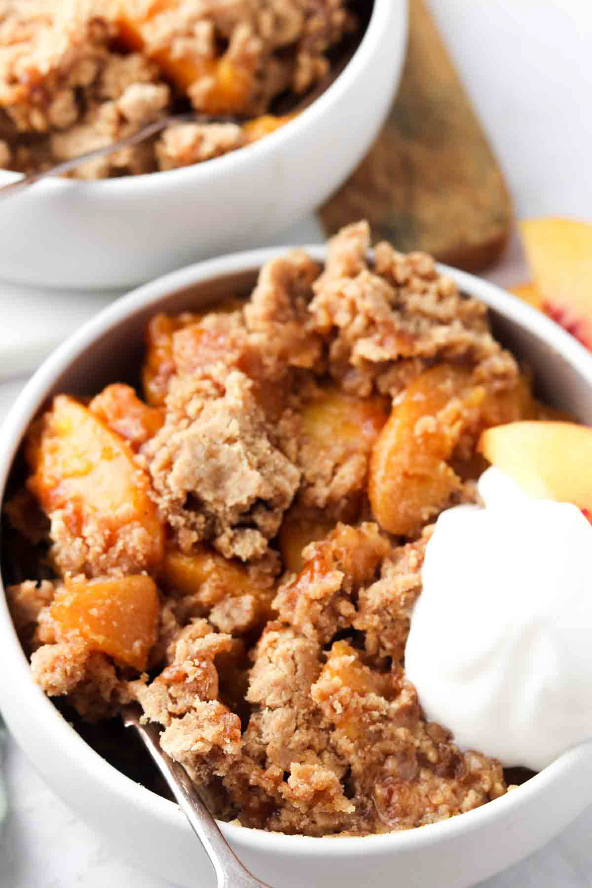 Peach cobbler in a white bowl with utensil inside dish.