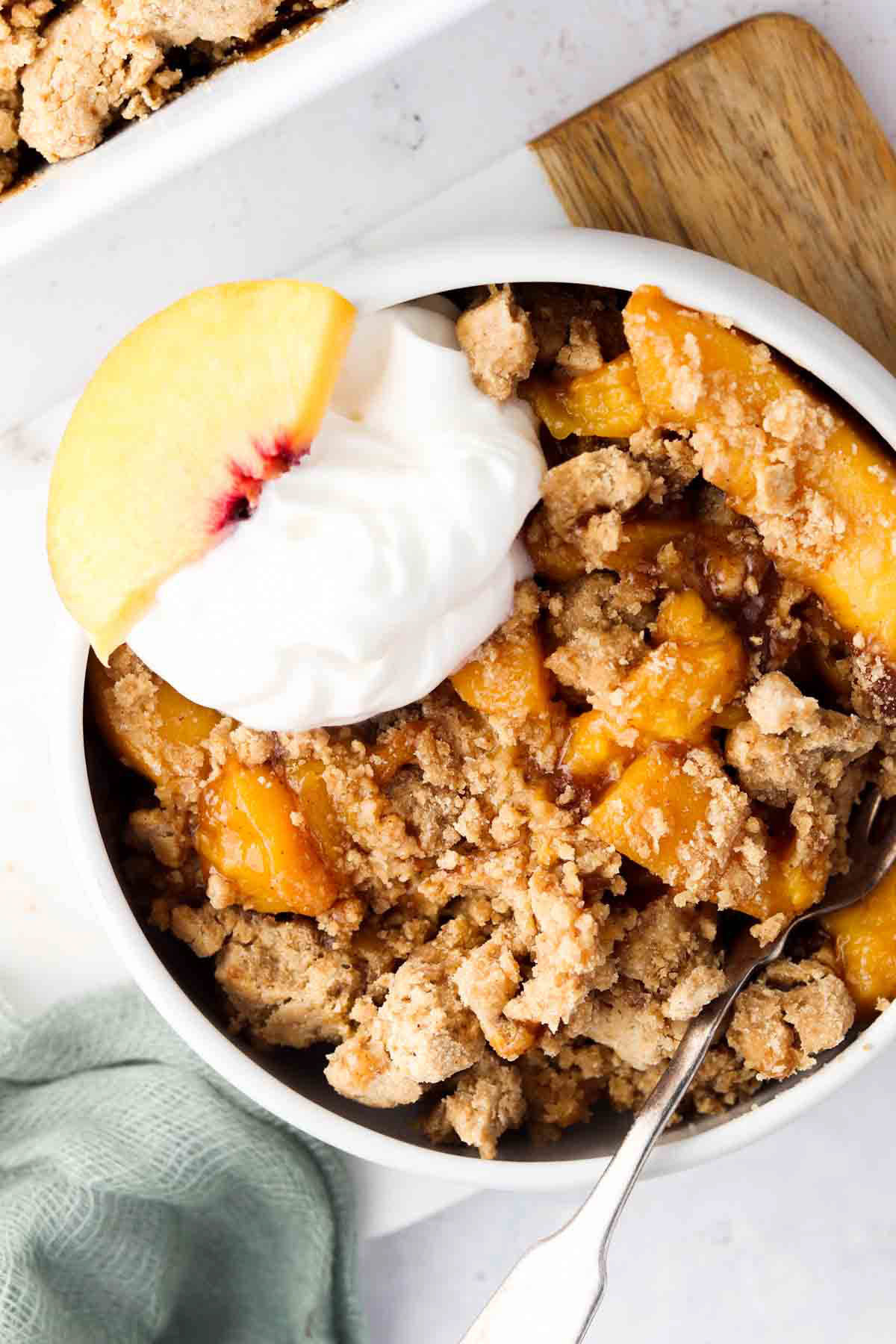 Peach cobbler in a serving dish with a spoonful of dairy free whipped cream and a peach slice.