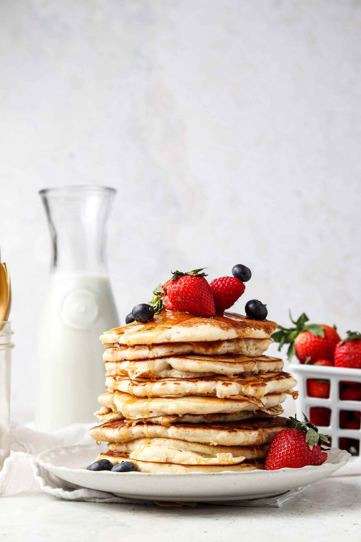 A stack of AIP pancakes on a plate with fresh strawberries and blueberries. 