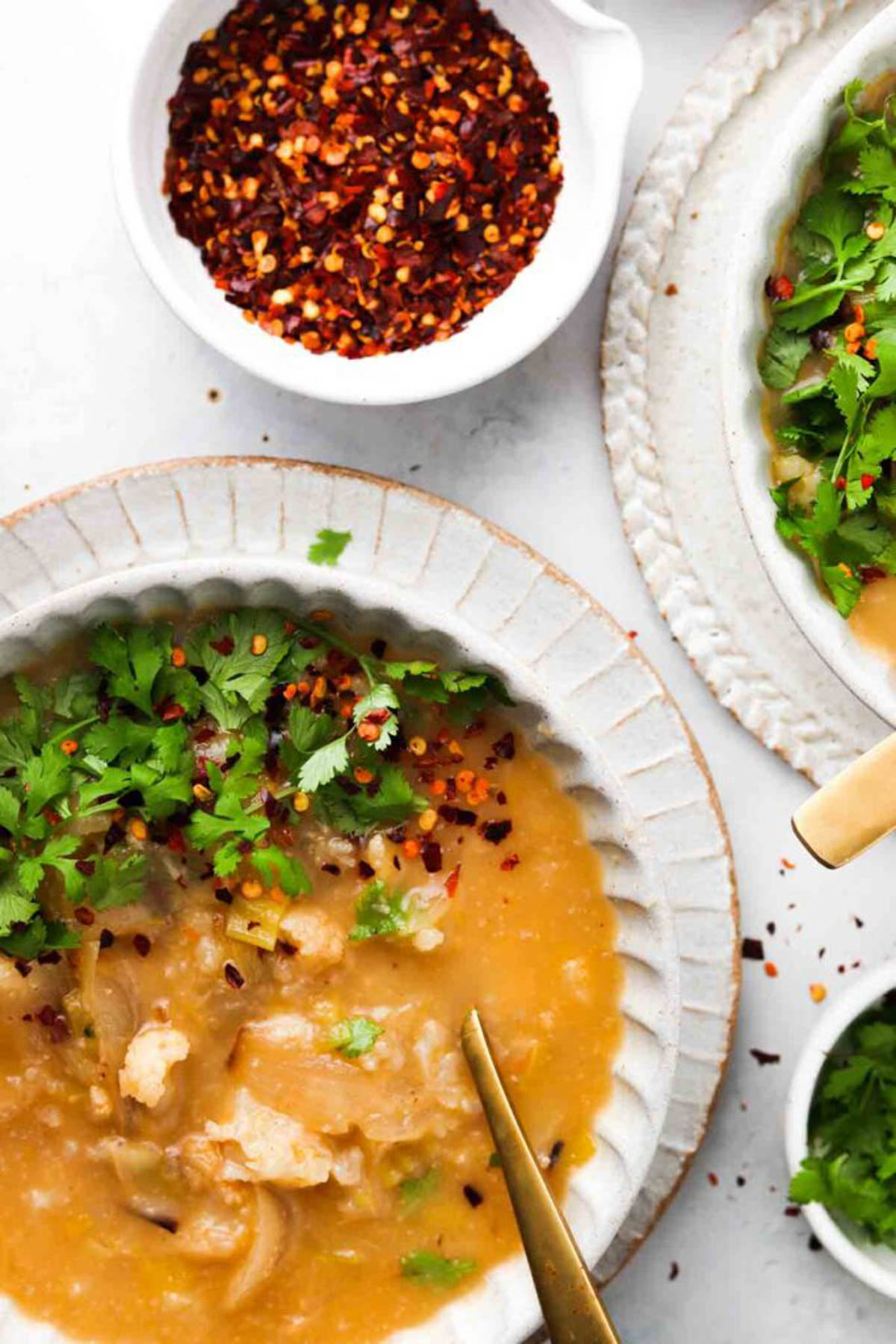 Cauliflower leek soup in a bowl and garnished with fresh green herbs and red pepper flakes.