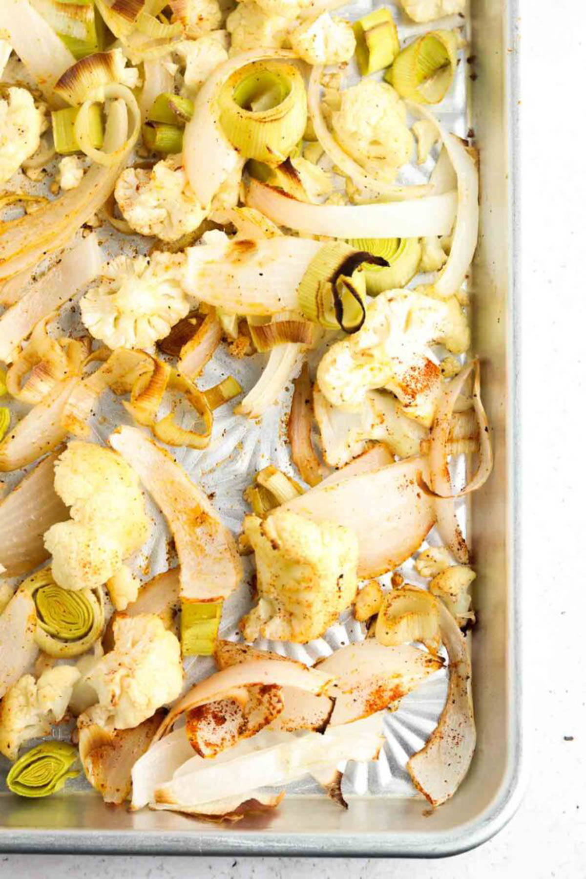 Roasted cauliflower, leeks, and onion on a sheet pan.