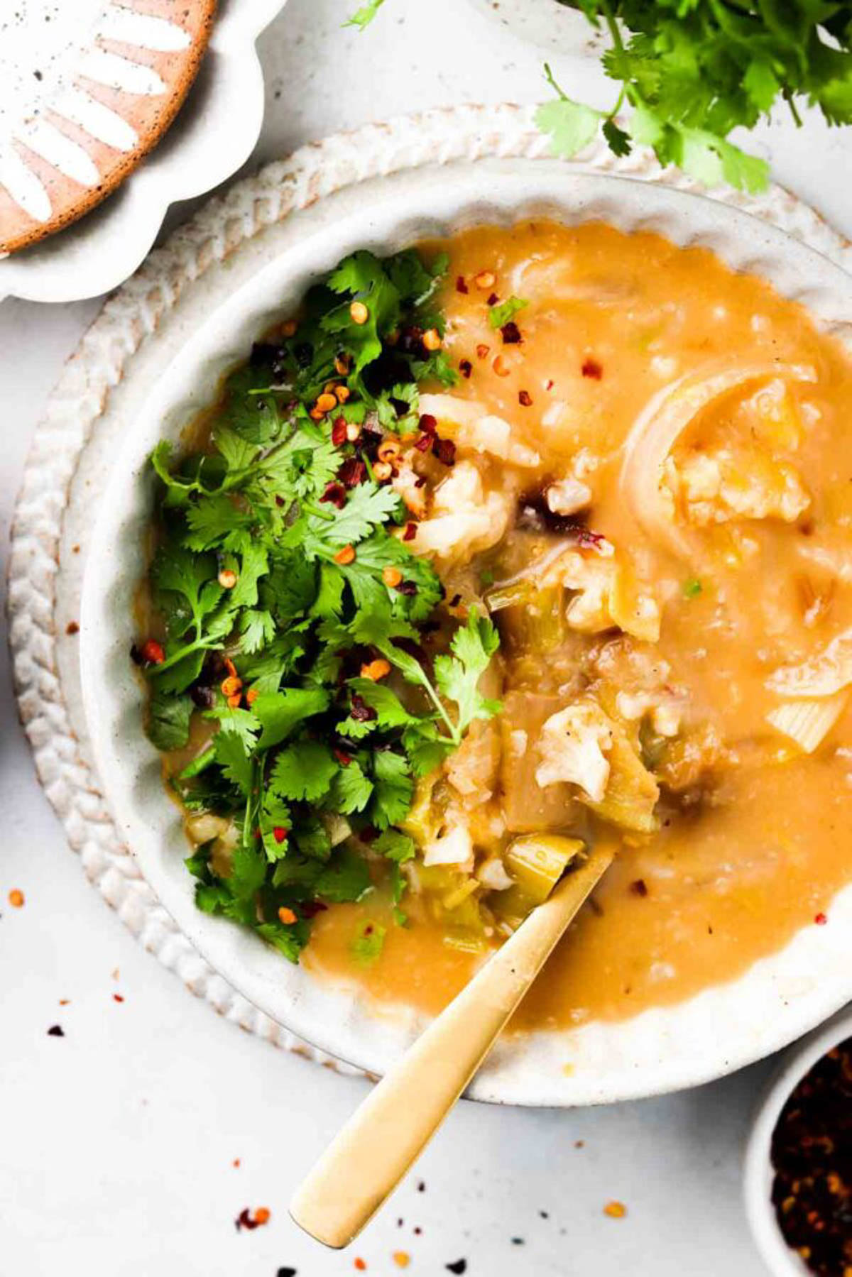 Chunky cauliflower leek soup in a bowl with golden spoon and garnished with fresh green herbs and red pepper flakes. 