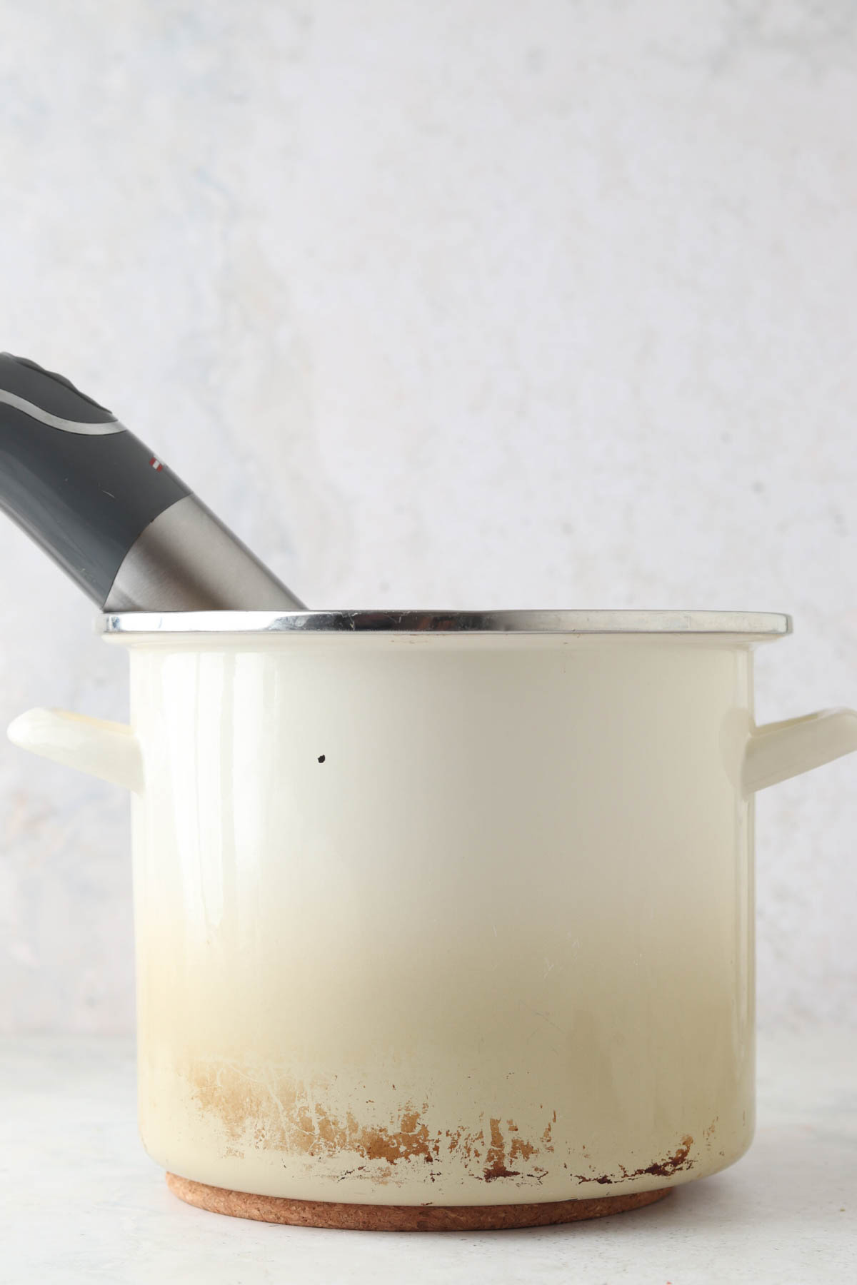 White stock pot with an immersion blender resting inside.