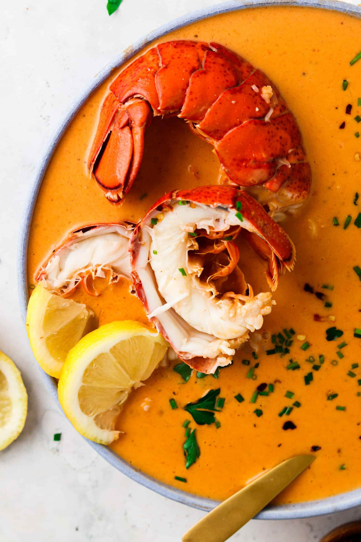 Dairy free lobster bisque in a bowl with fresh lemon and green herbs with a halved lobster tail.