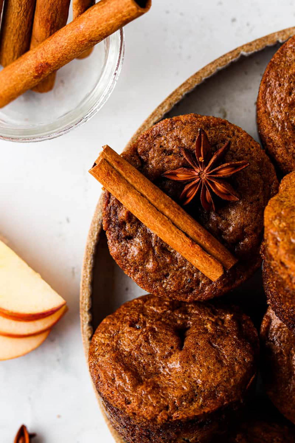 Gluten free apple muffins on a plate and garnished with whole cinnamon sticks and cloves.