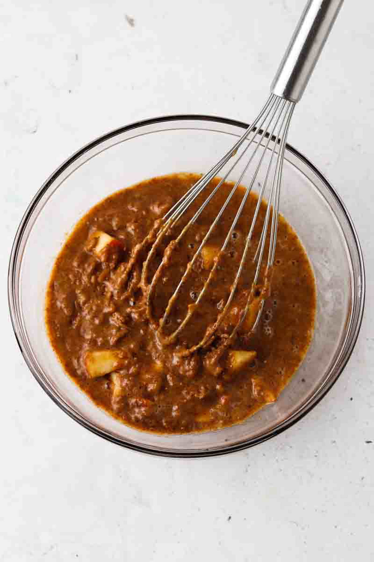 Gluten free apple muffin batter combined in a glass mixing bowl with a whisk.