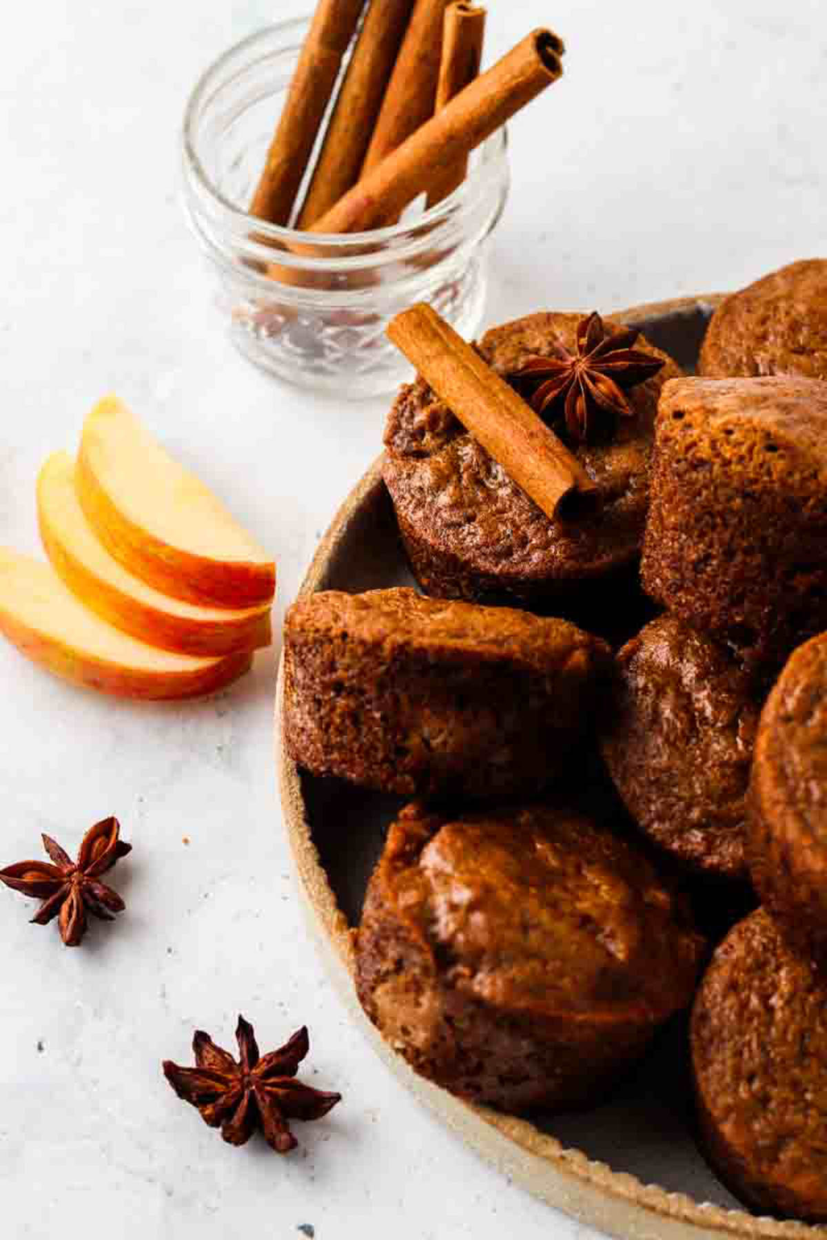 Gluten free apple muffins stacked on a plate and garnished with whole cloves, cinnamon sticks, and sliced apples.