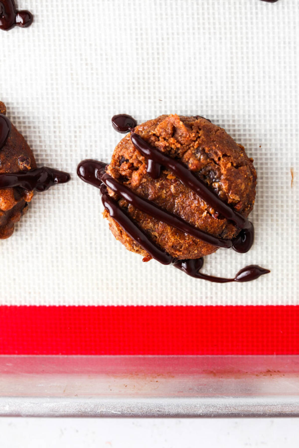 Gluten free pumpkin cookies on a silicone baking mat drizzled with chocolate.