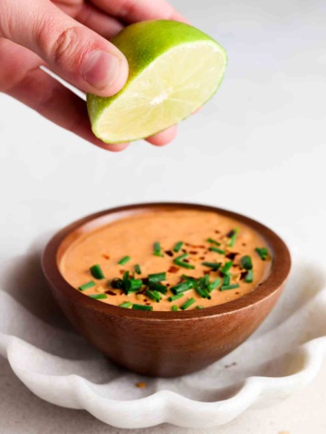 Orange sauce in a wooden bowl with red pepper flakes and fresh chives on top.