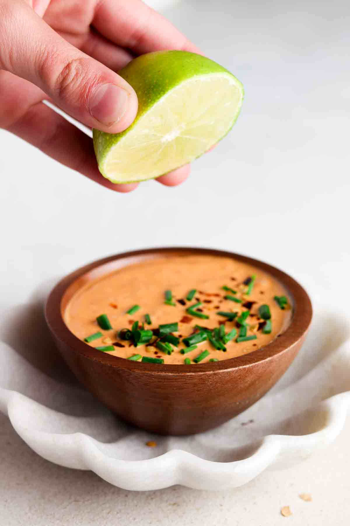 Orange sauce in a wooden bowl with red pepper flakes and fresh chives on top.