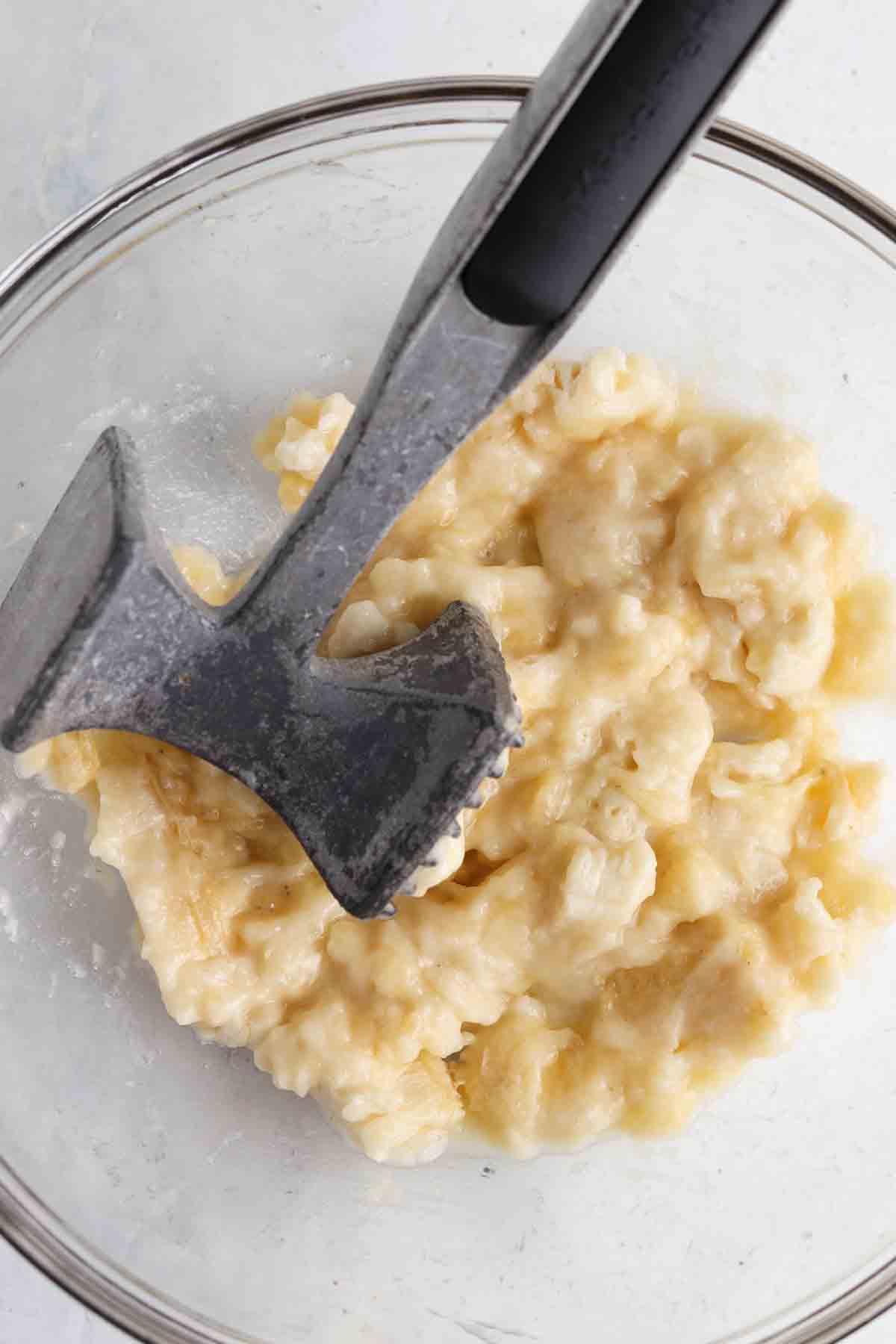 Mashed banana in a glass bowl with a potato masher.