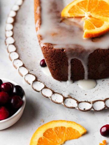 Orange cake on a scalloped white platter with white chocolate and orange slices on top.