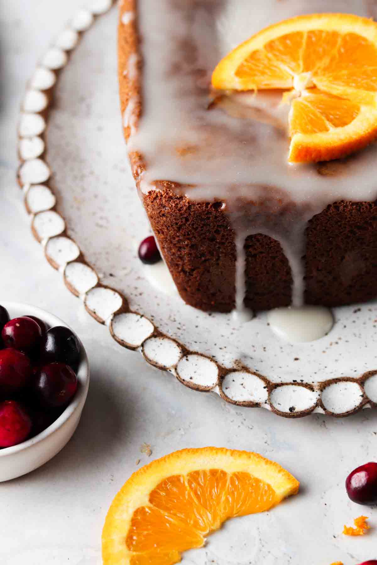 Orange cake on a scalloped white platter with white chocolate and orange slices on top.