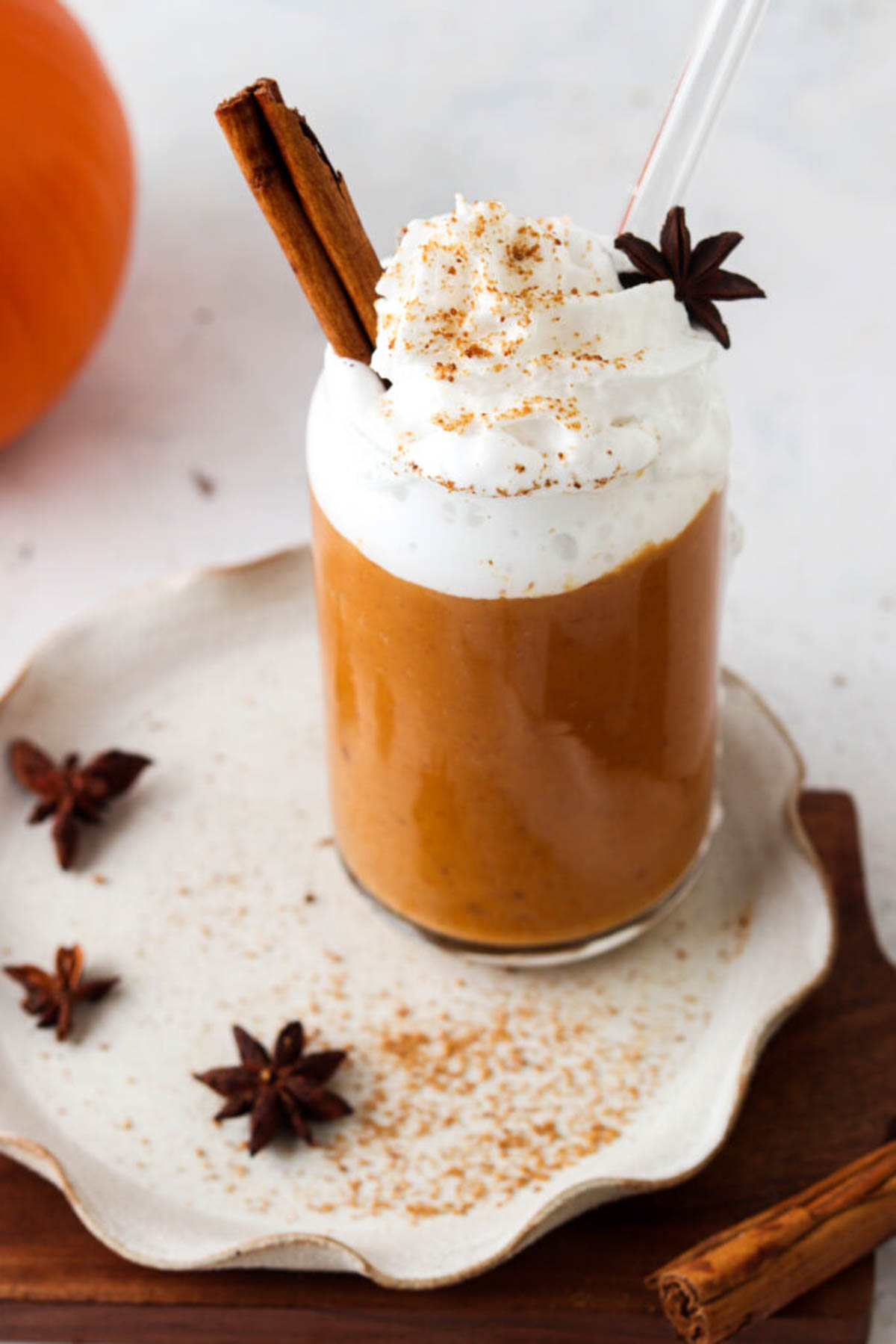 Dairy free pumpkin spice smoothie in a glass cup on a clay plate.