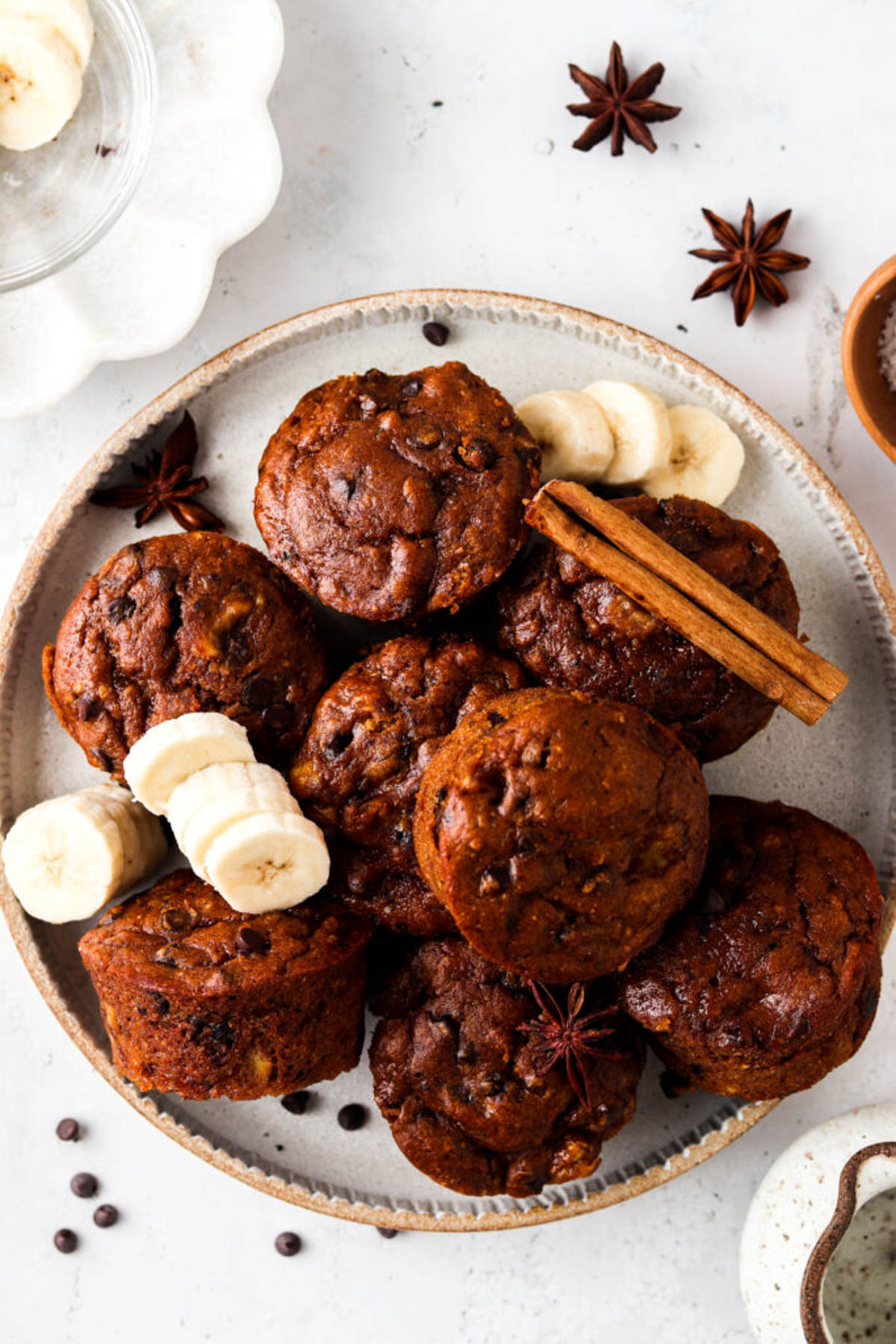 Gluten free pumpkin muffins piled on a plate and garnished with fresh banana and whole cinnamon sticks and star anise.