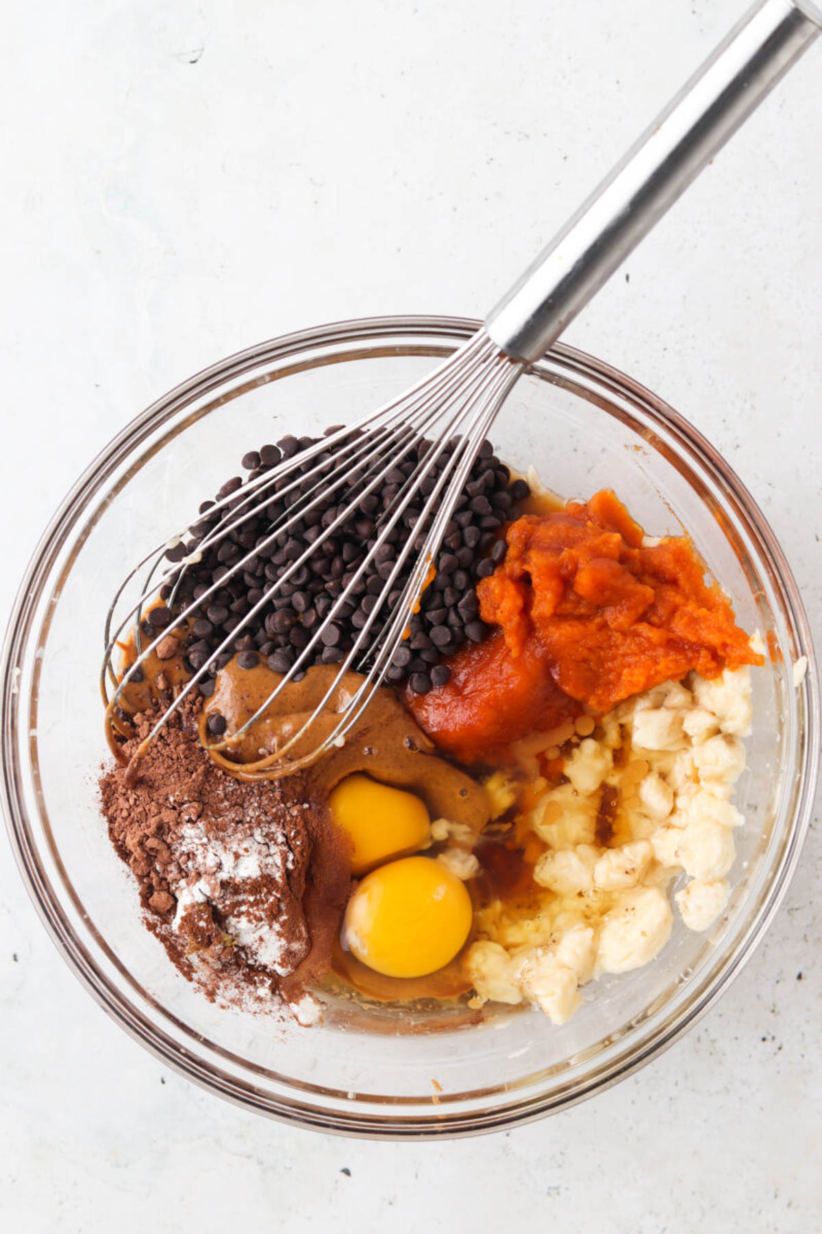 Gluten free pumpkin muffin ingredients in a glass bowl with mashed banana and a whisk.