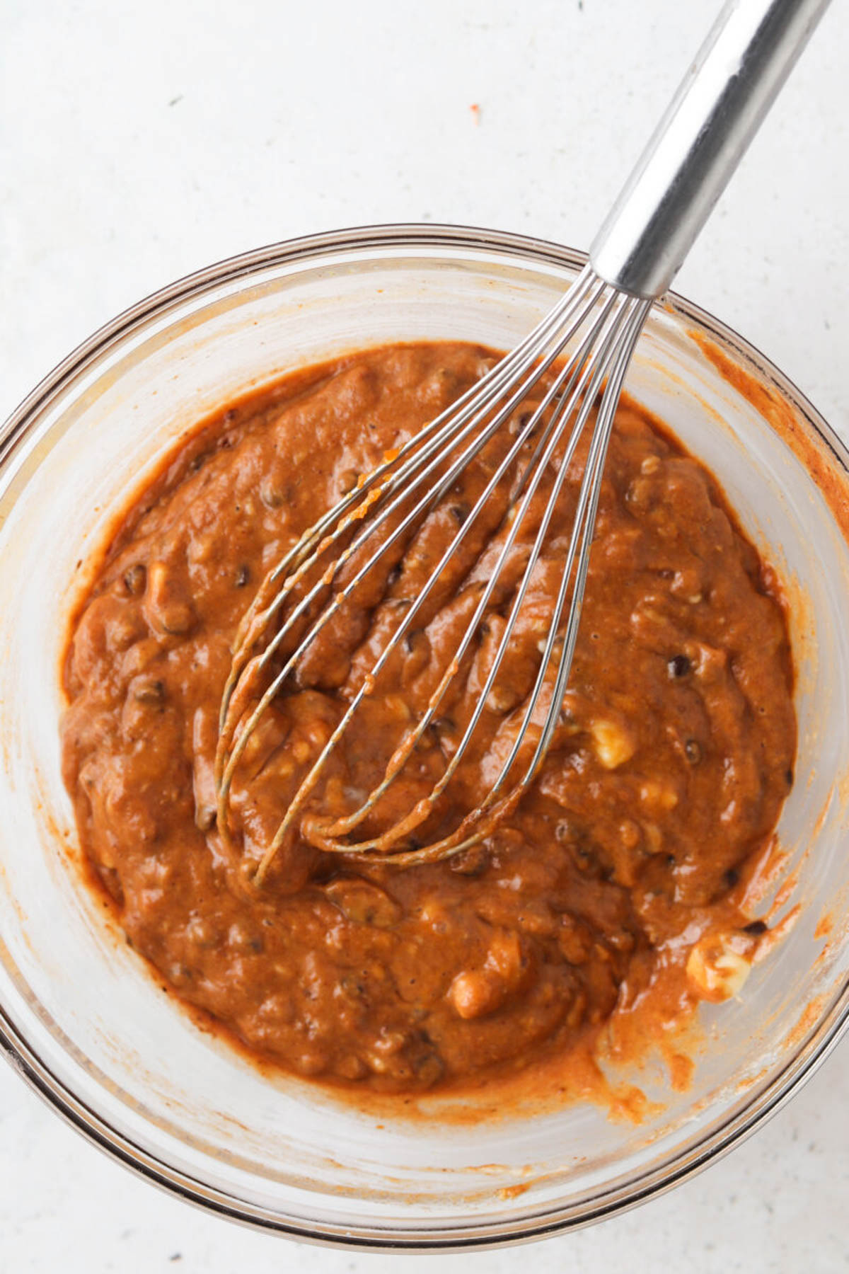 Raw gluten free pumpkin muffin batter in a glass bowl with a whisk.