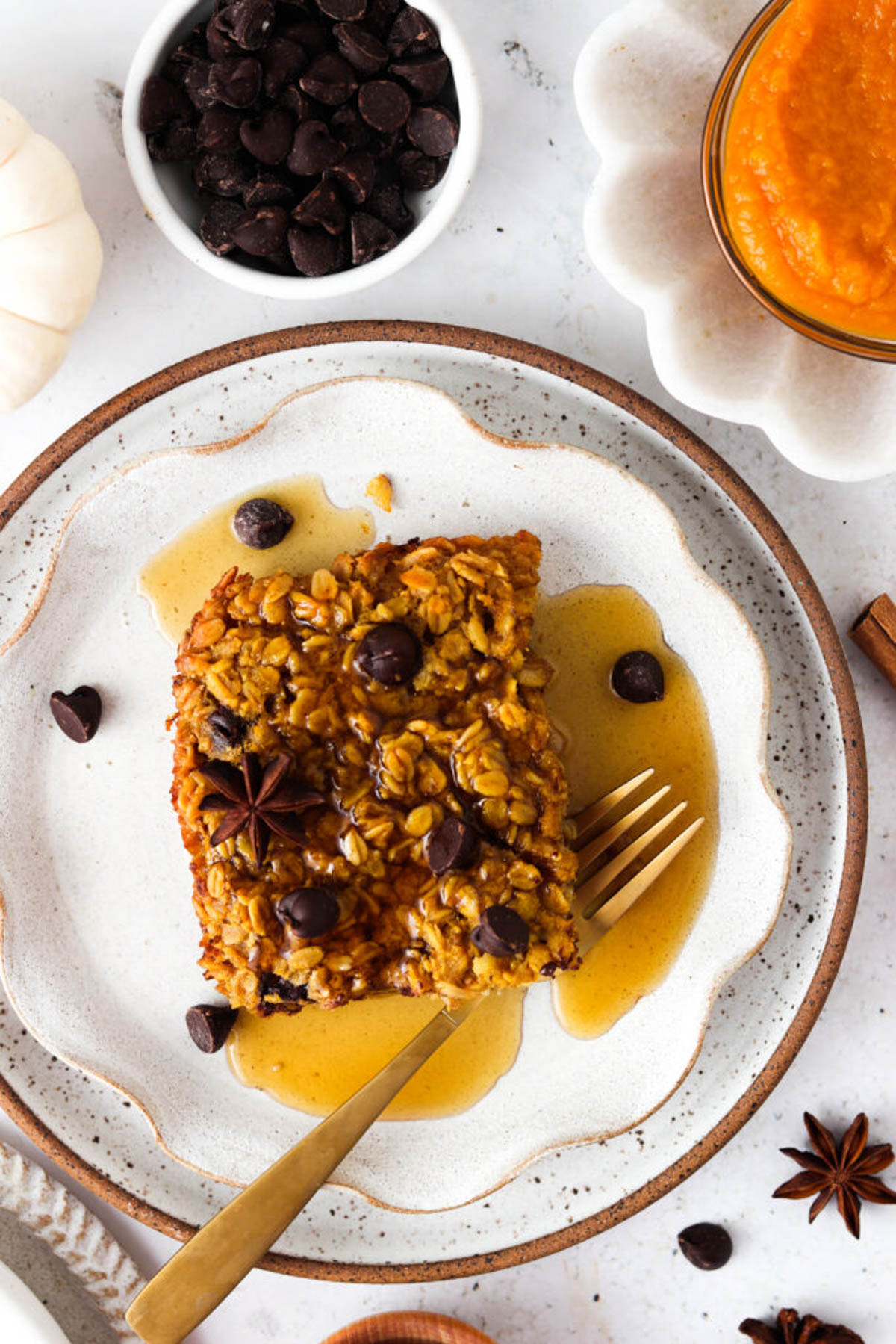 Pumpkin baked oatmeal on a plate with maple syrup and extra chocolate chips.