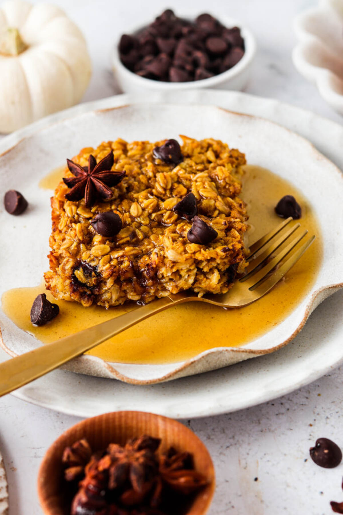 Pumpkin baked oatmeal slice on a plate with a gold fork and maple syrup.