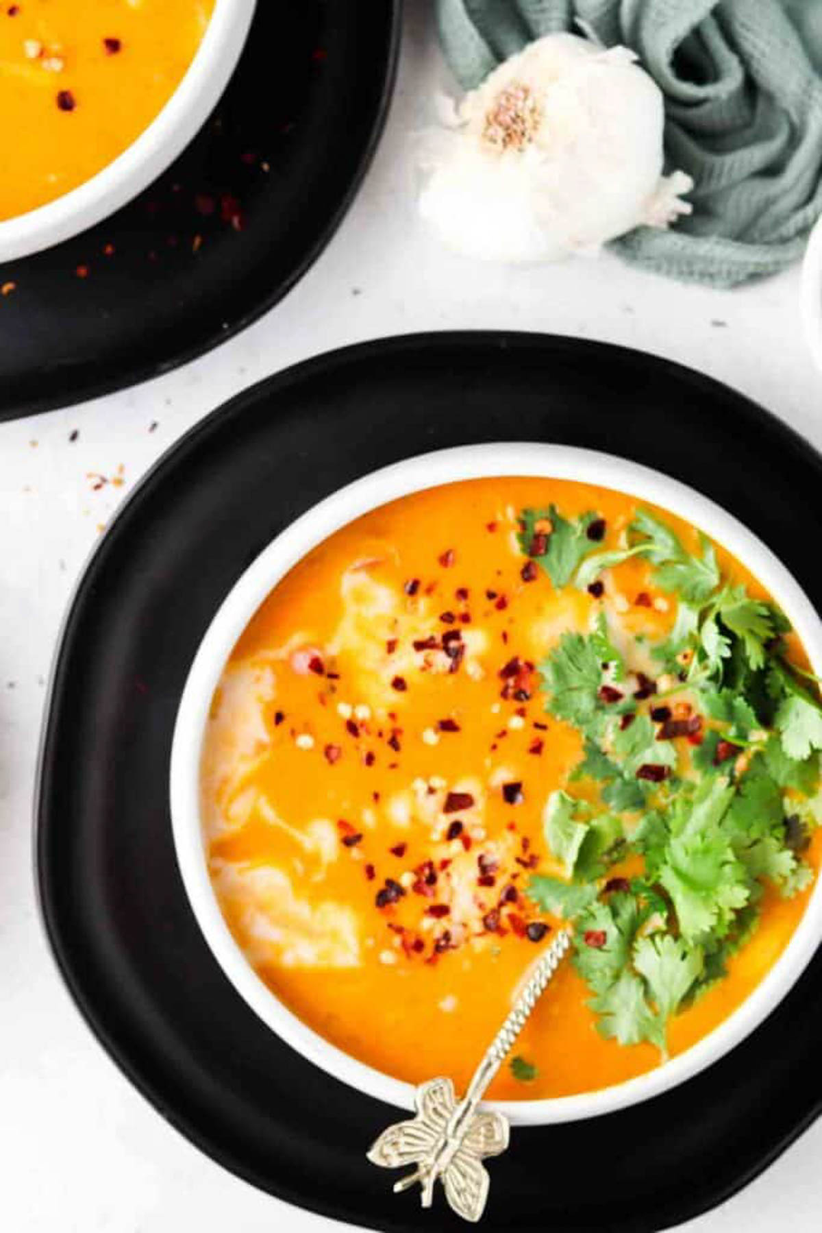 Pumpkin slow cooker soup in a white bowl on a black plate and garnished with fresh green herbs. 