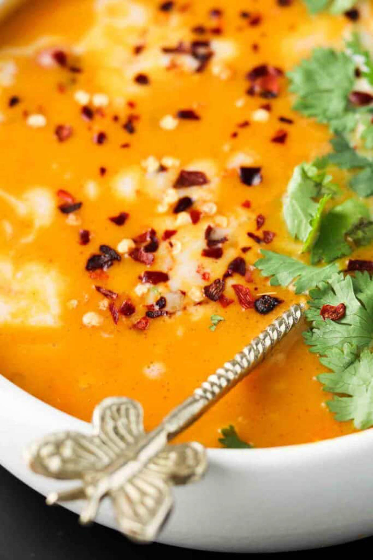 Slow cooker pumpkin soup in a white bowl with fresh green herbs garnishing the bowl. 