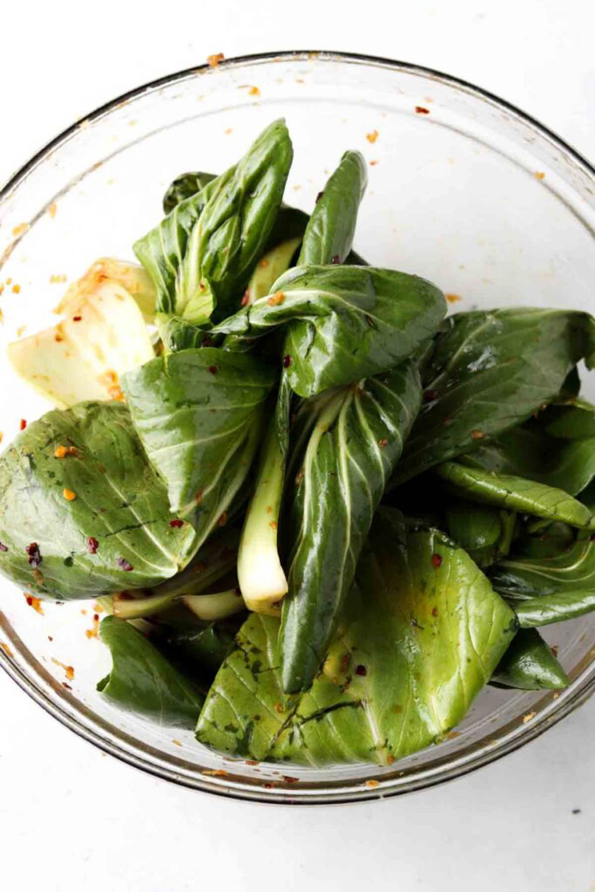 Bok choy leaves in a glass bowl with marinade poured over. 