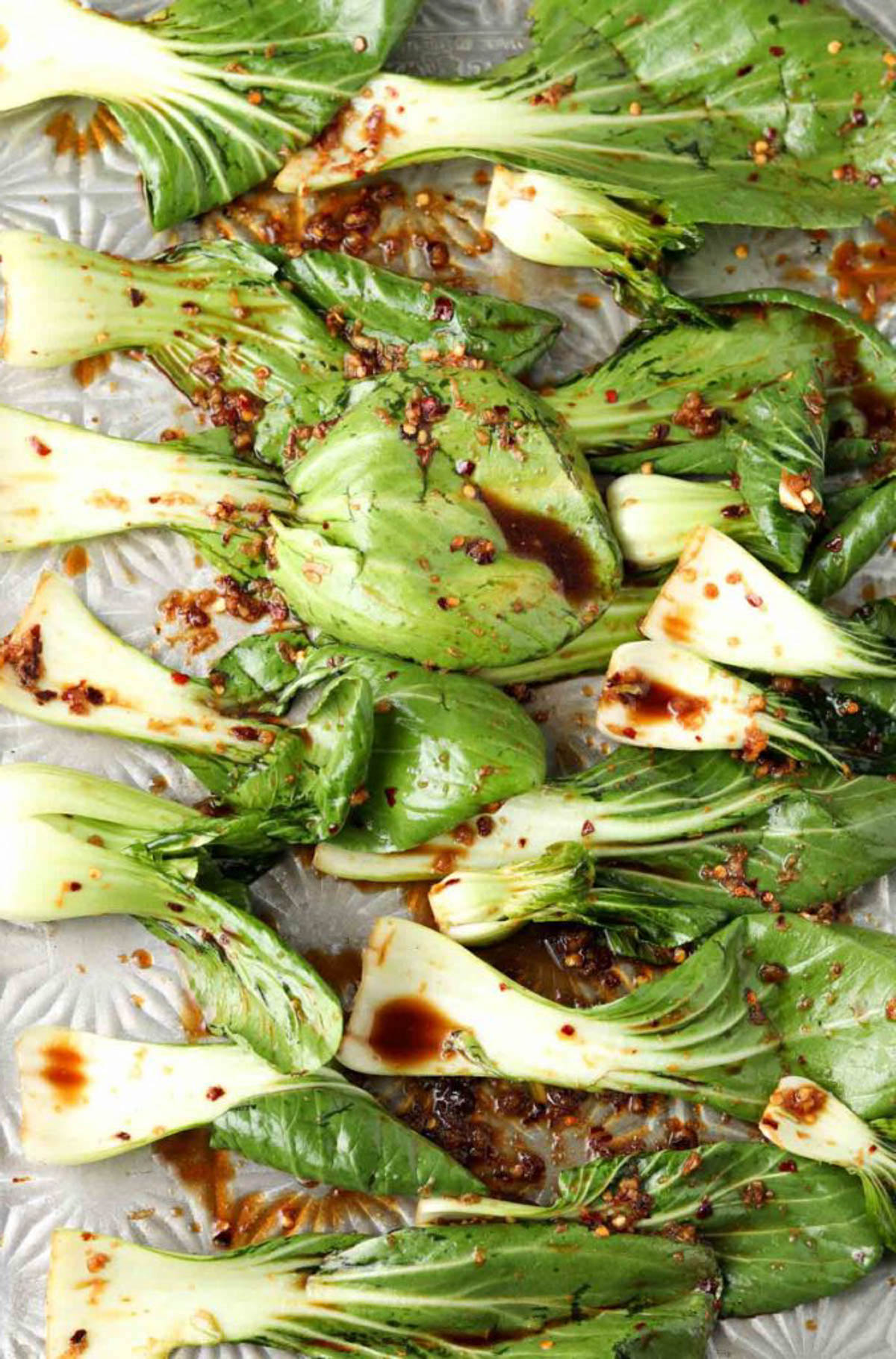 Uncooked bok choy on a baking sheet with marinade poured over. 