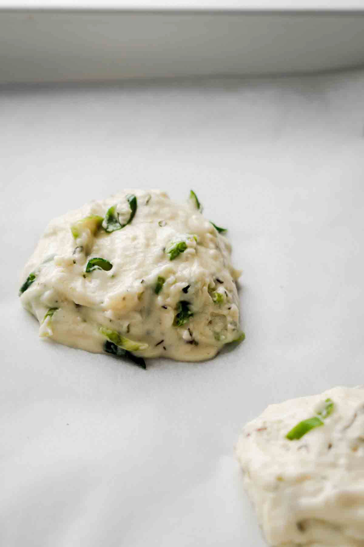 Raw aip bread roll dough scooped onto parchment lined baking sheet. 