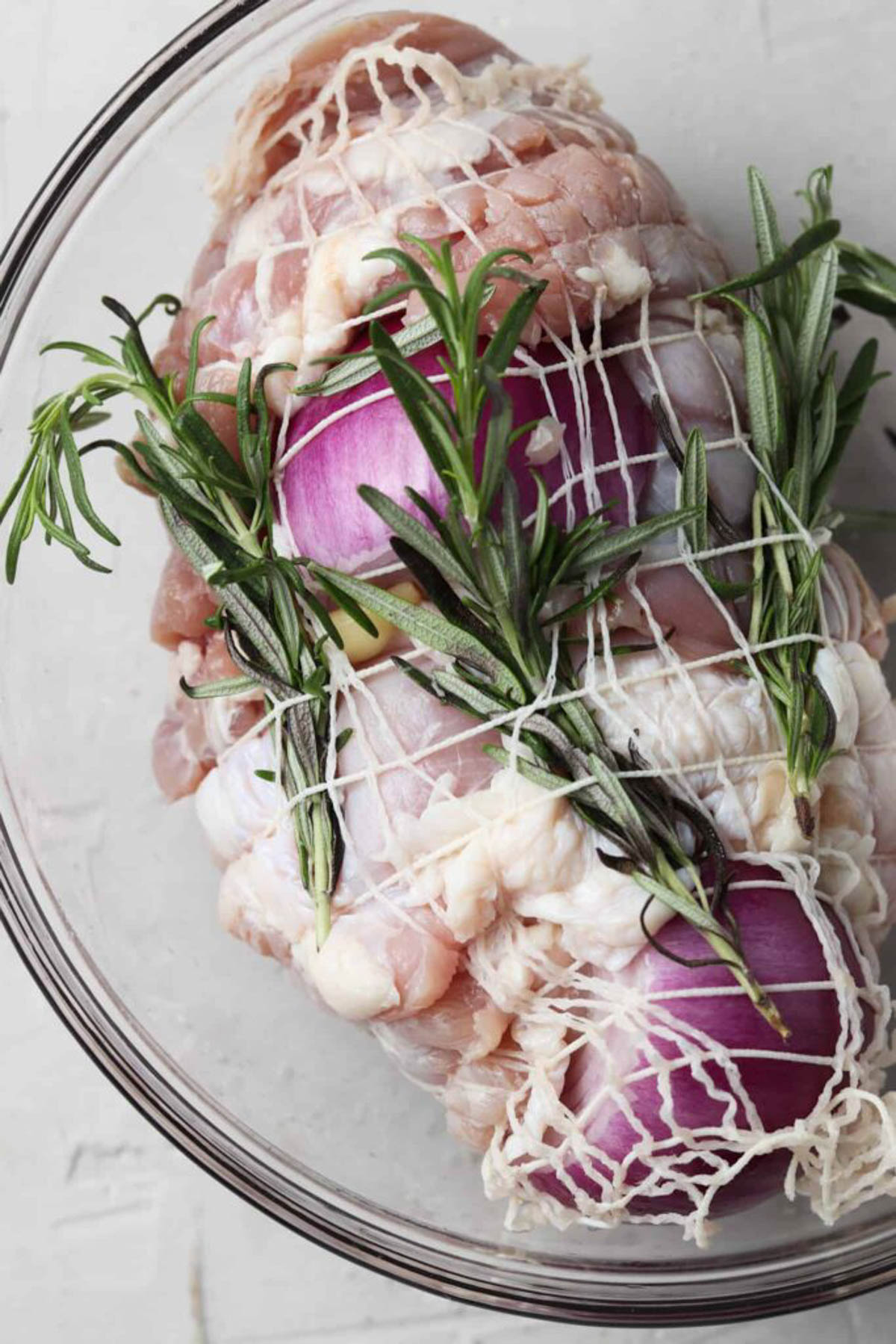 Raw turkey breast in a glass bowl with raw red onion and fresh rosemary.