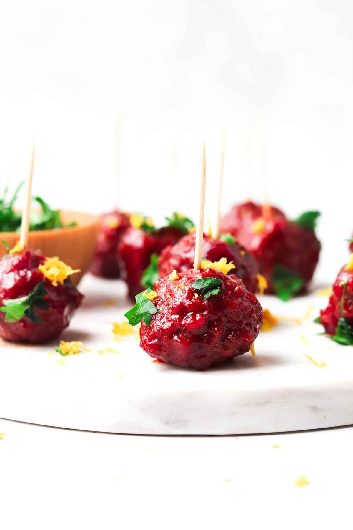 Cranberry BBQ meatballs garnishes with fresh green herbs and citrus zest with a toothpick in them.