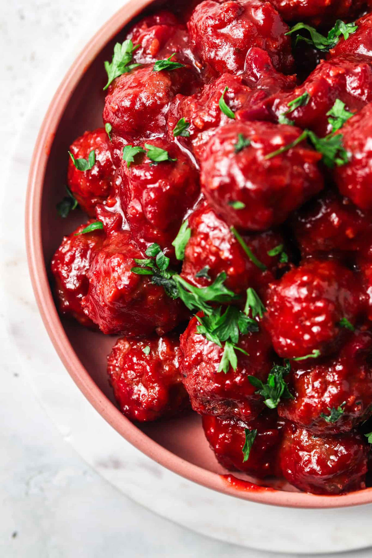 Cranberry BBQ Meatballs on a pink plate and garnished with fresh herbs.