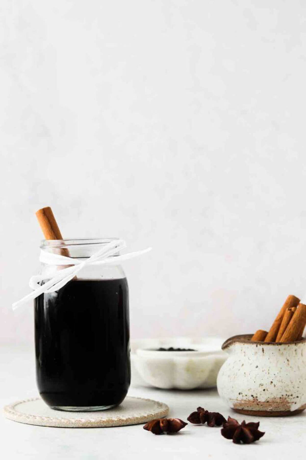 Homemade elderberry syrup in a glass mason jar with a cinnamon stink resting inside.