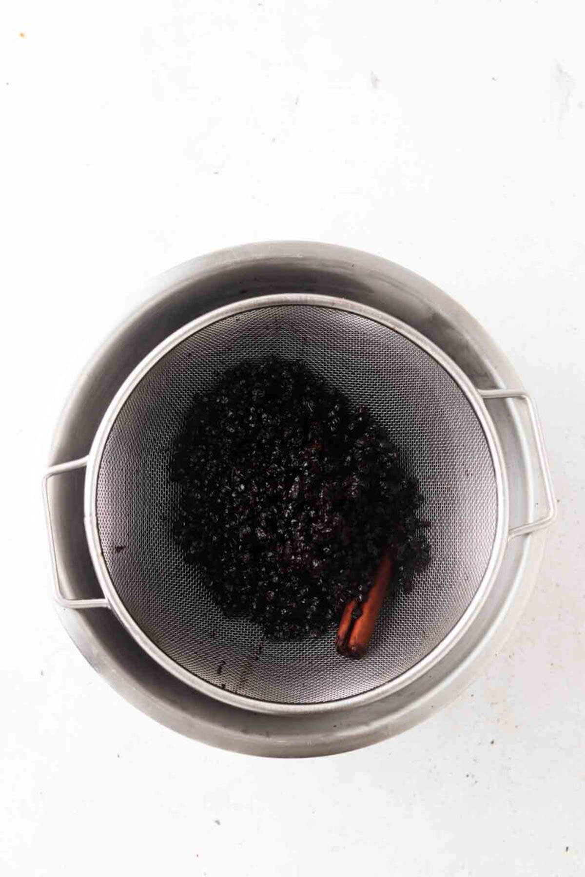 Homemade elderberry syrup being drained in a strainer.