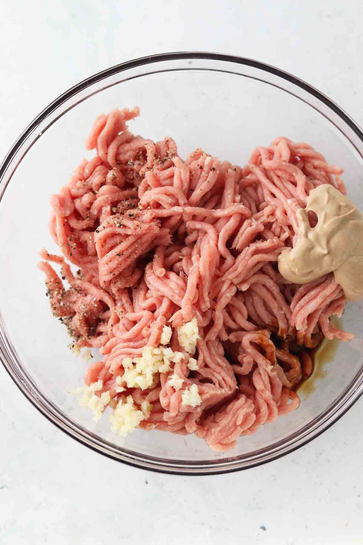 Ground turkey, garlic, Worcestershire sauce, dijon mustard, sea salt, and black pepper in a glass mixing bowl.