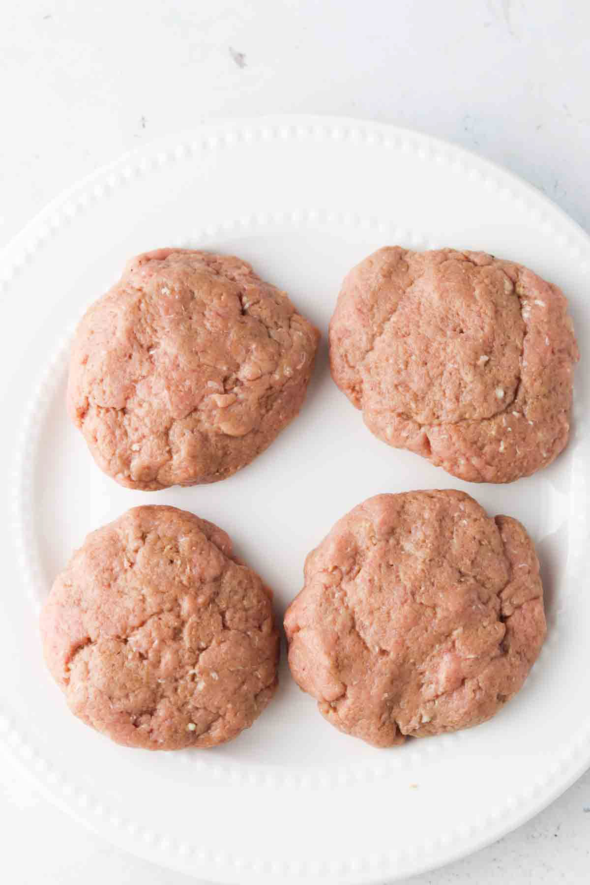 Shaped turkey burger patties on a white plate.