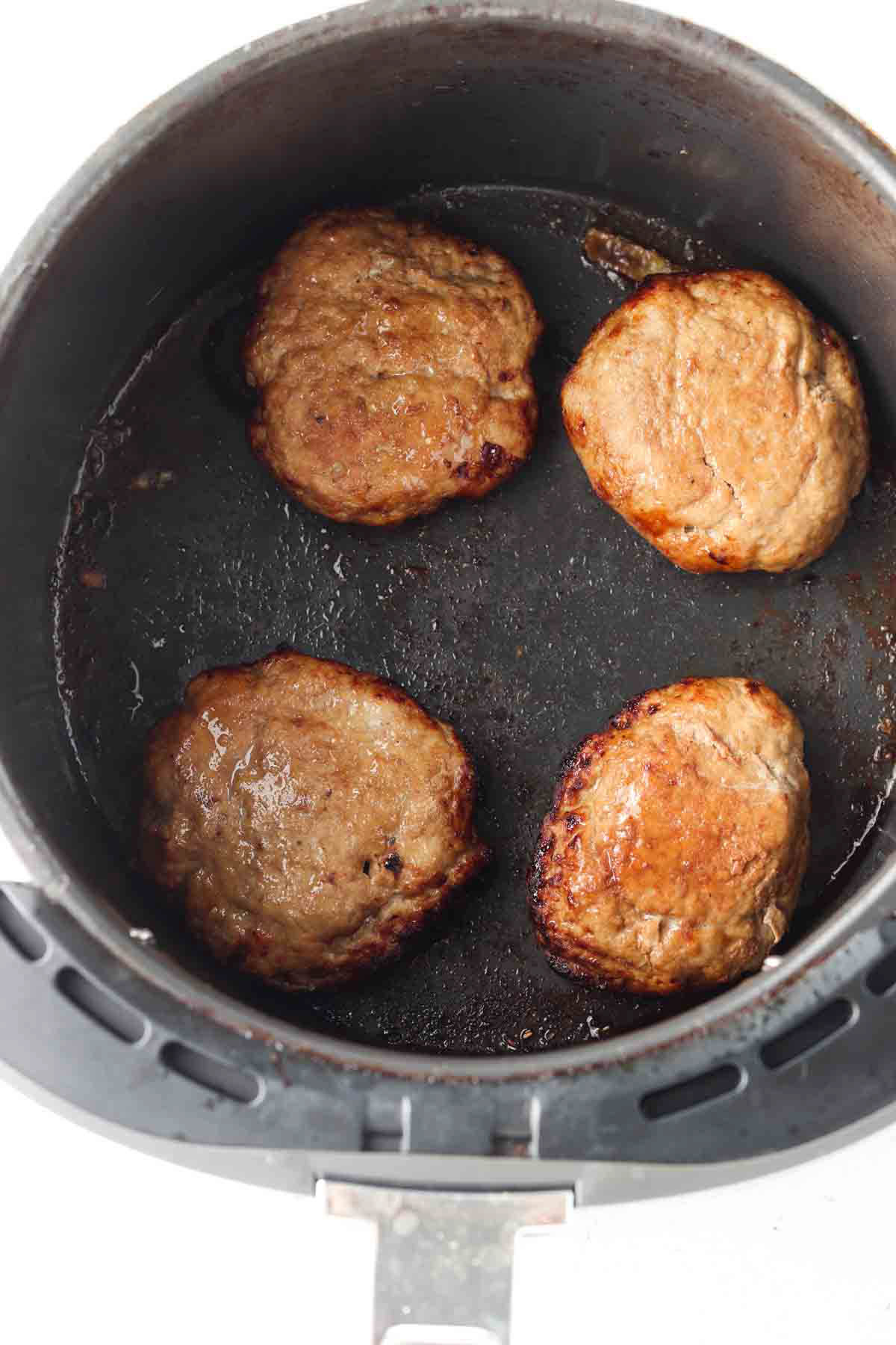 Cooked turkey burgers in an air fryer base.