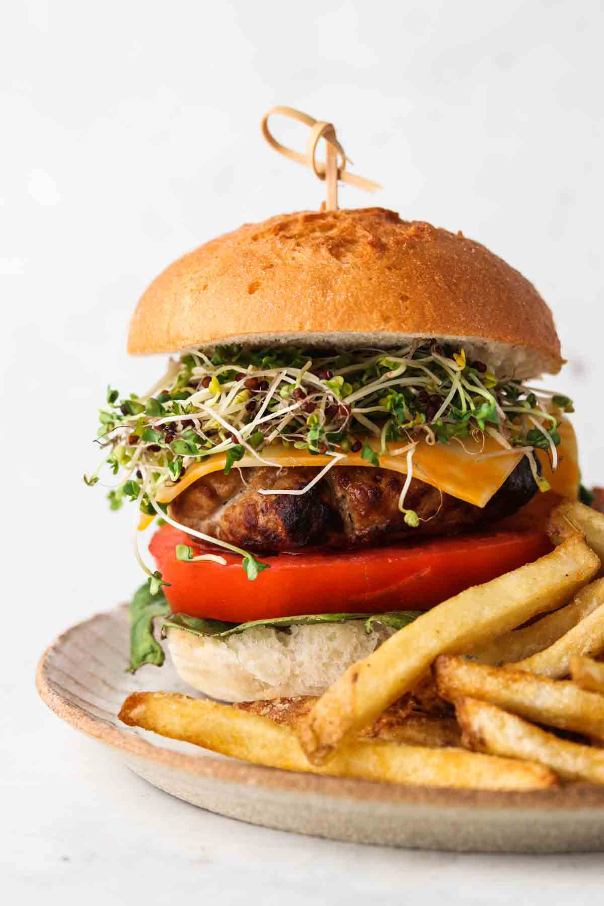 An air fried turkey burger on a plate with a toothpick holding it together and french fries.