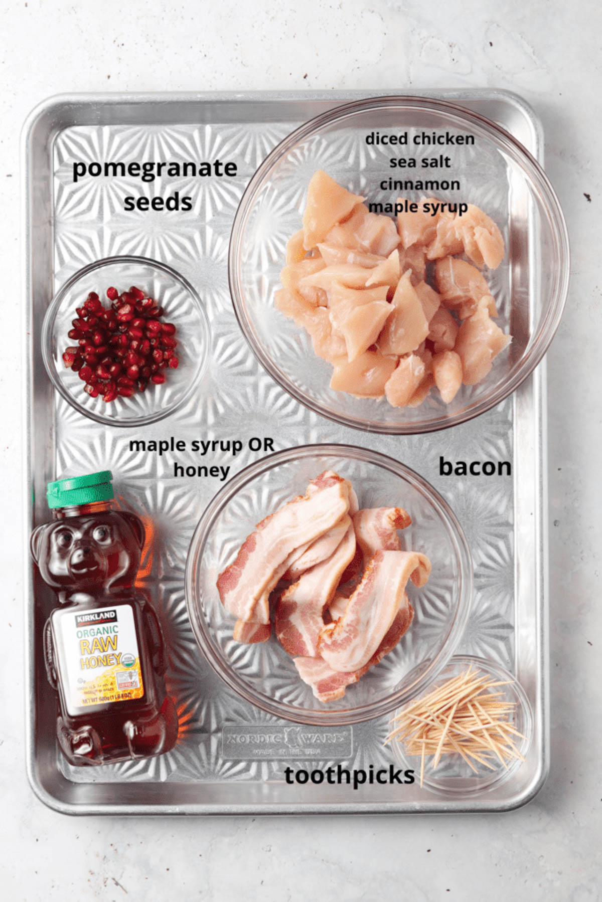 Bacon wrapped chicken bite ingredients in glass containers on a metal tray.